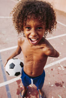 Porträt eines Jungen, der einen Fußball auf einem Fußballfeld hält - LJF00981
