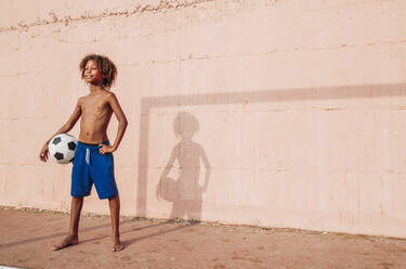 Smiling boy holding a soccer ball standing on a soccer field - LJF00984