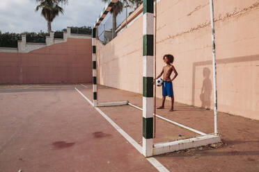 Boy holding a soccer ball standing on a soccer field - LJF00985