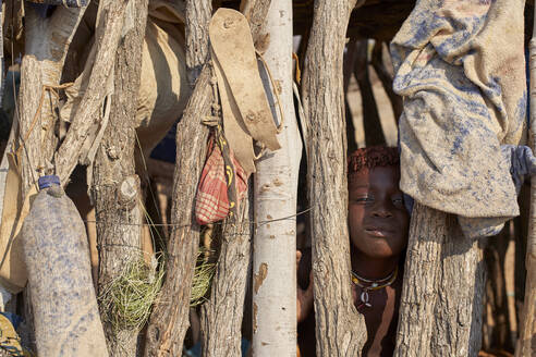 Mucubal-Mädchen versteckt sich hinter einem Holzzaun, Tchitundo Hulo, Virei, Angola - VEGF00612