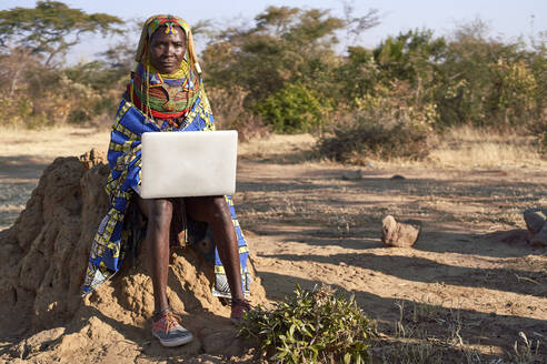 Traditionelle Muhila-Frau, mit Turnschuhen, arbeitet an ihrem Laptop, Kehamba, Chibia, Angola - VEGF00629
