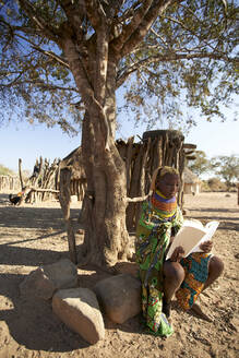 Traditionelle Muhila-Frau, unter einem Baum sitzend, ein Buch lesend, Kehamba, Chibia, Angola - VEGF00631