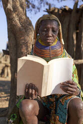 Traditionelle Muhila-Frau, unter einem Baum sitzend, ein Buch lesend, Kehamba, Chibia, Angola - VEGF00632