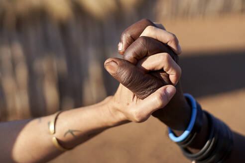 Traditionelle Muhacaona-Frau und weiße Frau halten sich an den Händen, Oncocua, Angola - VEGF00639