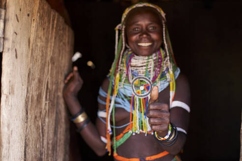 Porträt einer traditionellen Muhila-Frau, die in ihrem Haus steht und Brüste hochhält, Congolo, Angola - VEGF00648