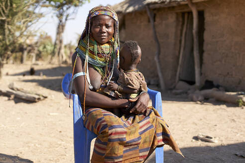 Traditionelle Muhila-Frau auf einem blauen Stuhl sitzend, mit Baby auf dem Schoß, Congolo, Angola. - VEGF00653