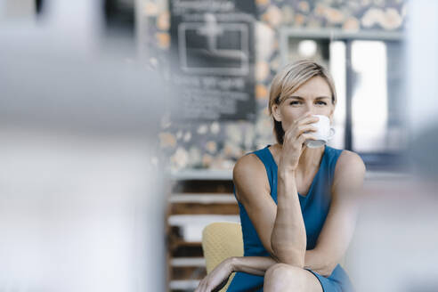 Woman drinking coffee in a coffee shop - KNSF06317