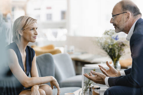 Businessman and woman having a meeting in a coffee shop, discussing work - KNSF06327