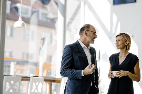 Businessman and woman talking about solutions, drinking coffee - KNSF06353