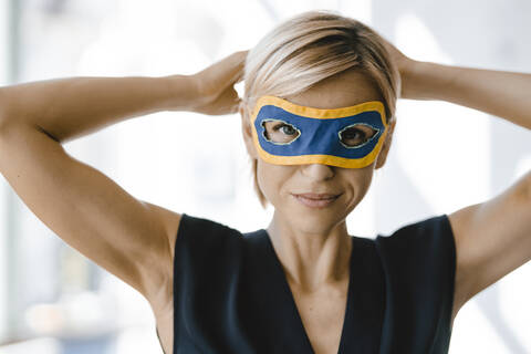 Porträt einer blonden Geschäftsfrau, die eine Superwoman-Maske trägt, lizenzfreies Stockfoto