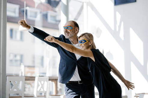 Businessman and woman wearing super hero masks, pretending to fly - KNSF06358