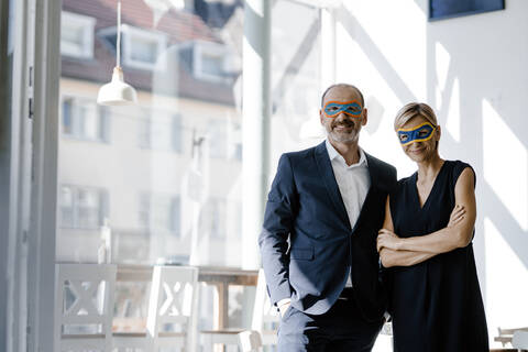 Businessman and woman wearing super hero masks, standing in coffee shop stock photo
