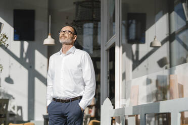 Businessman stansing in front of coffee shop, enjoying sunshine - KNSF06365