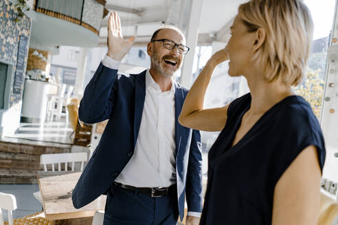 Business people high fiving in a coffee shop - KNSF06372