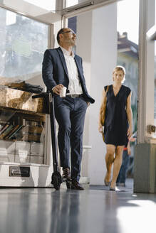 Businessman with e-scooter leaning in open door of a coffee shop - KNSF06376