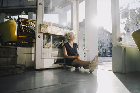 Businesswoman in coffee shop, sitting on skateboard, relaxing - KNSF06377