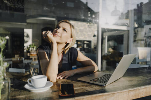 Blond woman using laptop in a coffee shop - KNSF06386