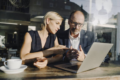 Businessman and woman sitting in coffee shop, using laptop - KNSF06387