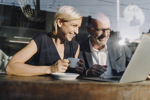 Businessman and woman sitting in coffee shop, using laptop - KNSF06388