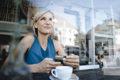 Businesswoman taking a break in coffee shop, holding smartphone - KNSF06402