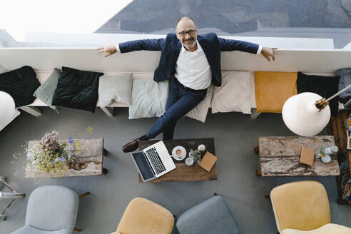 Businessman sitting relaxed in coffee shop, overhead view - KNSF06412