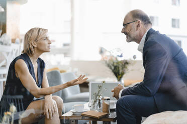 Businessman and woman having a meeting in a coffee shop, discussing work - KNSF06417