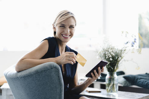 Businesswoman making online payment, using smartphone and credit card in a coffe shop - KNSF06420