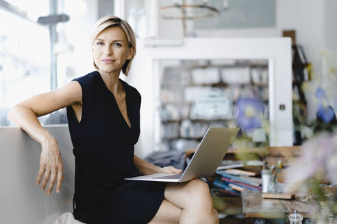 Businesswoman sitting in coffee shop, using laptop - KNSF06421