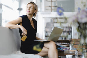 Businesswoman making online payment, sitting in coffee shop, using laptop and credit card - KNSF06422