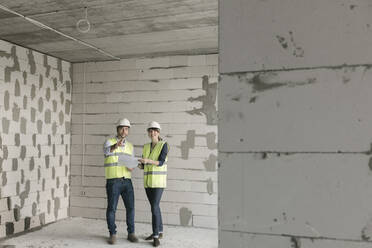 Two architects talking about architectural plan while standing at construction site - AHSF00805