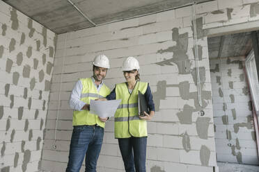 Zwei Architekten, die auf einer Baustelle stehend einen Bauplan prüfen - AHSF00806