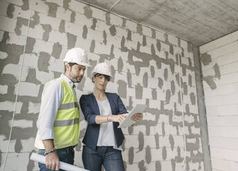 Two architects using tablet while standing at construction site - AHSF00809