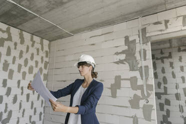 Female architect checking architectural plan on construction site - AHSF00813