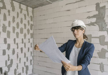 Female architect checking architectural plan on construction site - AHSF00839