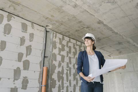 Architektin prüft Bauplan auf der Baustelle, lizenzfreies Stockfoto