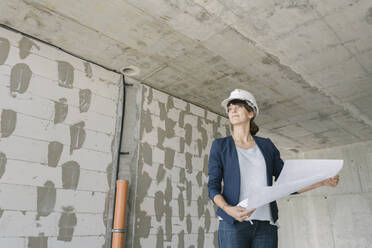 Female architect checking architectural plan on construction site - AHSF00846