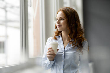 Porträt einer rothaarigen Geschäftsfrau mit Kaffee zum Mitnehmen, die aus dem Fenster schaut - KNSF06436