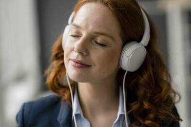 Porträt einer rothaarigen Geschäftsfrau, die mit weißen Kopfhörern Musik hört - KNSF06437