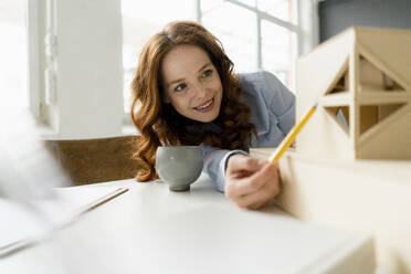 Portrait of smiling redheaded woman looking at architectural model - KNSF06442