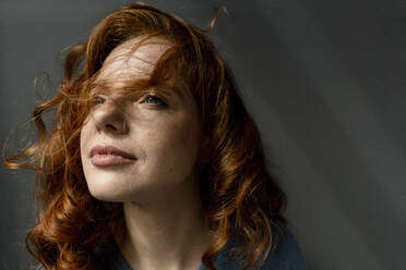 Portrait of daydreaming redheaded woman against grey background - KNSF06461