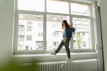 Rothaarige Frau balanciert auf der Heizung in einem Dachgeschoss - KNSF06472