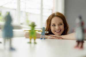 Porträt einer lächelnden rothaarigen Geschäftsfrau in einem Loft mit Miniaturrobotern auf dem Schreibtisch - KNSF06480