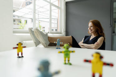 Porträt einer rothaarigen Frau in einem Loft mit Miniaturrobotern auf dem Schreibtisch - KNSF06483