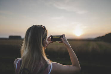 Frau, die mit ihrem Smartphone ein Foto vom Sonnenuntergang macht - CHPF00572