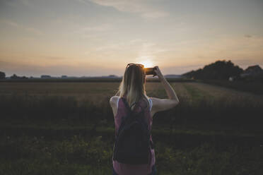 Frau, die mit ihrem Smartphone ein Foto vom Sonnenuntergang macht - CHPF00573