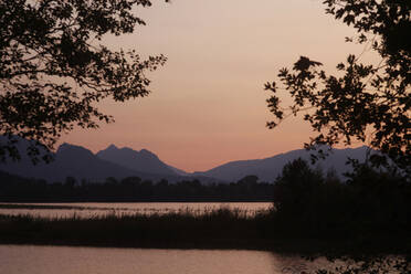 Blick auf den Forggensee und die Silhouette der Berge gegen den klaren Himmel bei Sonnenuntergang im Ostallgäu, Deutschland - JTF01298