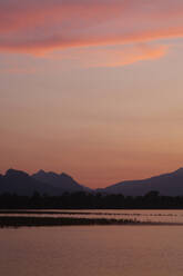 Scenic view of Forggensee lake and silhouette mountains against sky during sunset, Ostallgäu, Germany - JTF01302