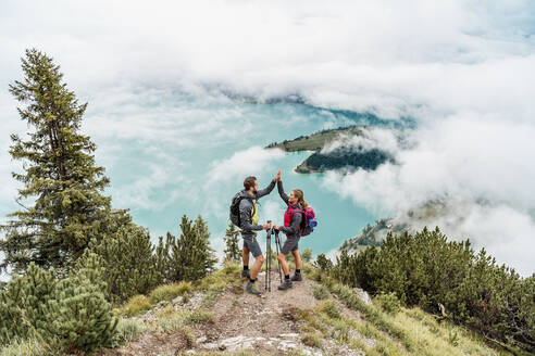 Happy young couple on a hiking trip in the mountains high fiving, Herzogstand, Bavaria, Germany - DIGF08274