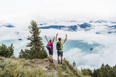 Happy young couple with raised arms on a hiking trip in the mountains, Herzogstand, Bavaria, Germany - DIGF08286