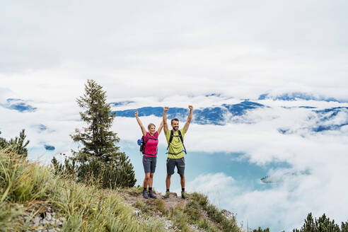 Happy young couple with raised arms on a hiking trip in the mountains, Herzogstand, Bavaria, Germany - DIGF08287